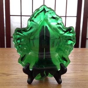 Peut inclure: Un plat en verre vert en forme de feuille sur un support noir. Le plat est en verre texturé et a une forme profonde et arrondie.