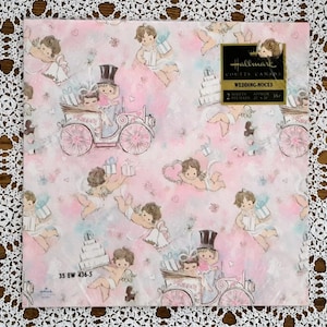 May include: Vintage Hallmark wrapping paper with a pink and white background featuring a repeating pattern of cherubs, hearts, and wedding cake designs. The paper is labelled "Wedding Noces" and "Coutts Canada".
