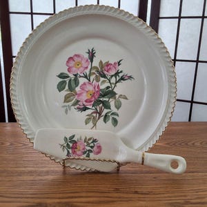 Peut inclure: Une assiette à gâteau blanche avec un bord doré et un motif floral avec des roses roses. Un serveur à gâteau assorti est inclus.