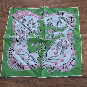 May include: A square green handkerchief with a playful design. A green figure with a pink nose holds a baton in the centre. The words "HOT TIME IN THE OLD TOWN TONIGHT" are written in pink around the figure. Musical notes and stars are scattered around the design.