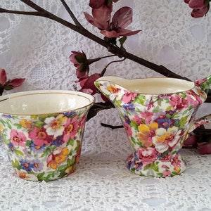 Peut inclure: Un ensemble sucrier et crémier vintage à fleurs. Les pièces sont blanches avec un motif floral dans les tons rose, jaune, bleu et vert. Le sucrier a un bord doré.