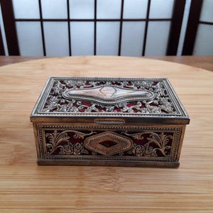 May include: An ornate silver and red jewellery box with a filigree design. The box has a hinged lid and a red velvet interior.