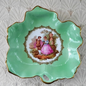 May include: A green porcelain leaf-shaped dish with a gold rim and a central oval design featuring a couple in a garden setting. The design is surrounded by a gold filigree border.