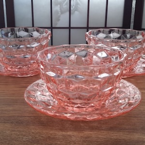 May include: Three pink glass bowls with matching pink glass saucers. The bowls and saucers have a diamond pattern.
