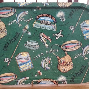 May include: Rectangular green metal tray with a fishing theme. The tray features illustrations of fish, fishing gear, and text including "Gone Fishing", "Fresh Catch Today", and "Fish Lake Lodge". The tray has a decorative handle.