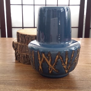 May include: A blue ceramic vase with a textured, abstract design in a light brown color. The vase has a wide base and a narrow neck.