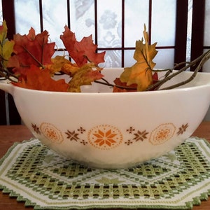 May include: A white ceramic mixing bowl with a brown and orange geometric pattern. The bowl is filled with autumn leaves and a branch.