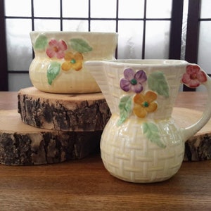 Peut inclure: Deux crémiers en céramique vintage avec des motifs floraux. Les crémiers sont blancs avec un glaçage jaune et présentent un motif de panier tissé. Les fleurs sont roses, jaunes, violettes et vertes.