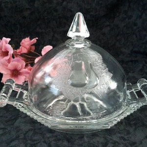 Peut inclure: Un beurrier en verre transparent avec un motif de poire. Le plat a deux poignées et un couvercle bombé avec un bouton.
