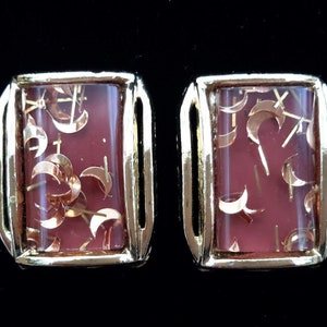 Peut inclure: Une paire de boucles d'oreilles dorées avec une pierre rectangulaire, rose, translucide remplie de paillettes dorées. Les paillettes sont en forme de croissants de lune et d'étoiles.