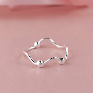 May include: A silver ring with a wavy band and three small round beads.