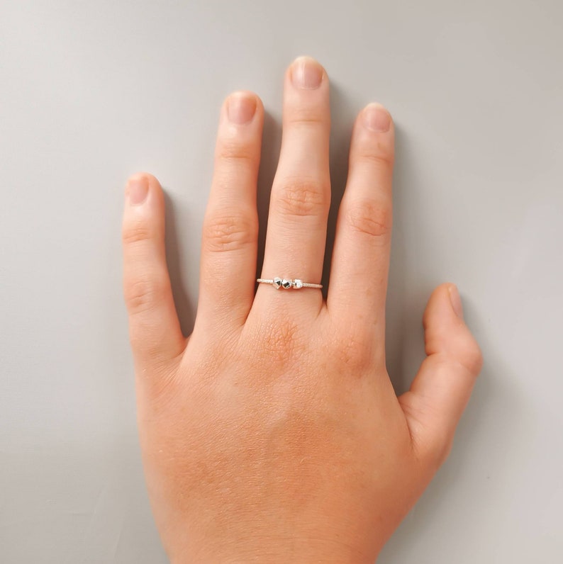 May include: A silver ring with three small, round beads on the band.