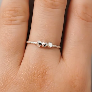 May include: A silver ring with three small, geometric-shaped beads.