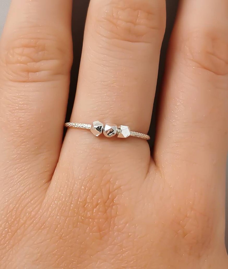 May include: A silver ring with three small, geometric-shaped beads.