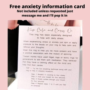 May include: A white card with pink text that reads "Free anxiety information card" and "Keep Calm and Carry On". The card explains how to use a fidget ring to help with stress and anxiety. It includes a tip on box breathing.