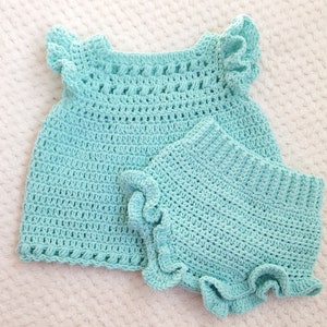 May include: A light blue crocheted baby outfit with a ruffled top and matching bloomers.