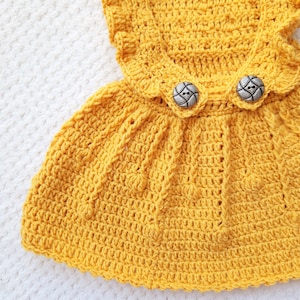 May include: A yellow crocheted dress with a ruffled neckline and two silver buttons.