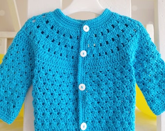 May include: A turquoise blue crocheted cardigan with white buttons. The cardigan has a simple design with a V-neck and long sleeves.