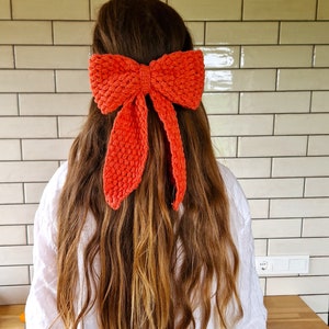 May include: A bright orange crocheted bow headband. The headband is tied in a bow and worn in the hair.