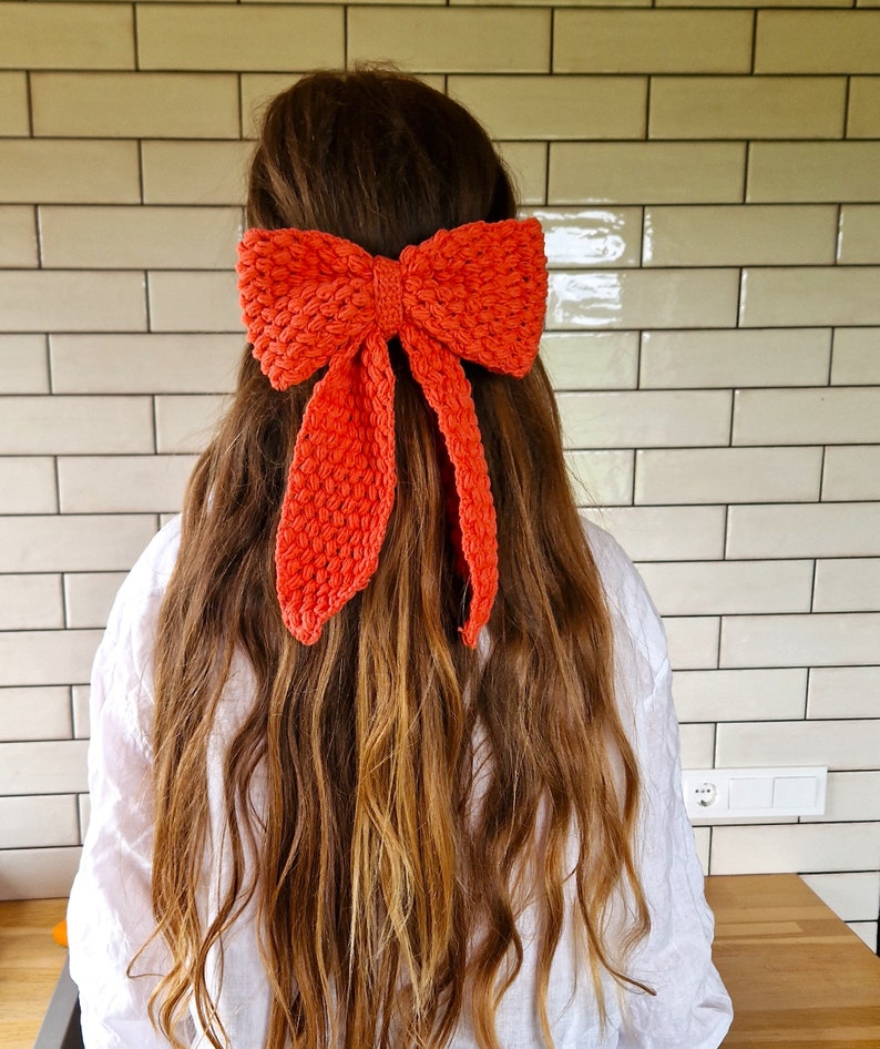 May include: A bright orange crocheted bow headband. The headband is tied in a bow and worn in the hair.