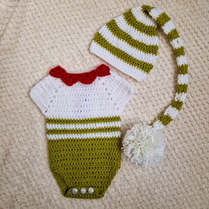 Peut inclure: Ensemble de bébé au crochet fait à la main, comprenant un body blanc et vert olive avec un col rouge et un chapeau rayé assorti avec une longue queue et un pompon blanc. L'ensemble est pour bébé.