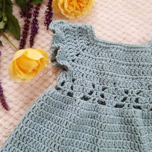 Peut inclure: Une robe de bébé en crochet bleu clair avec un délicat motif de dentelle autour du col et des manches.