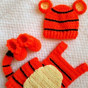 May include: A crocheted baby outfit in orange and black stripes with a matching hat and booties. The hat has large orange ears and the outfit has a yellow crocheted belly.