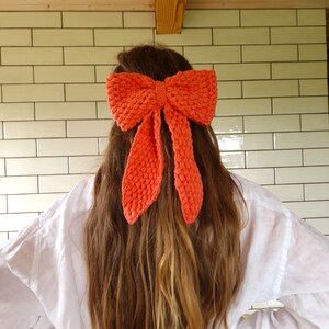 May include: A large, bright orange crocheted bow tied in the back of a person's hair.