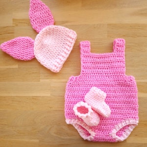 Könnte beinhalten: Rosa gestricktes Baby-Outfit mit passender Mütze und Booties. Das Outfit besteht aus einem ärmellosen Strampler mit einem gehäkelten Design und einer passenden Mütze mit Hasenohren.