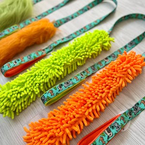 May include: Four dog toys with bright green and orange fuzzy textures. Each toy has a matching leash with a turquoise background and a pattern of cartoon koalas and other animals. The leashes have orange trim.