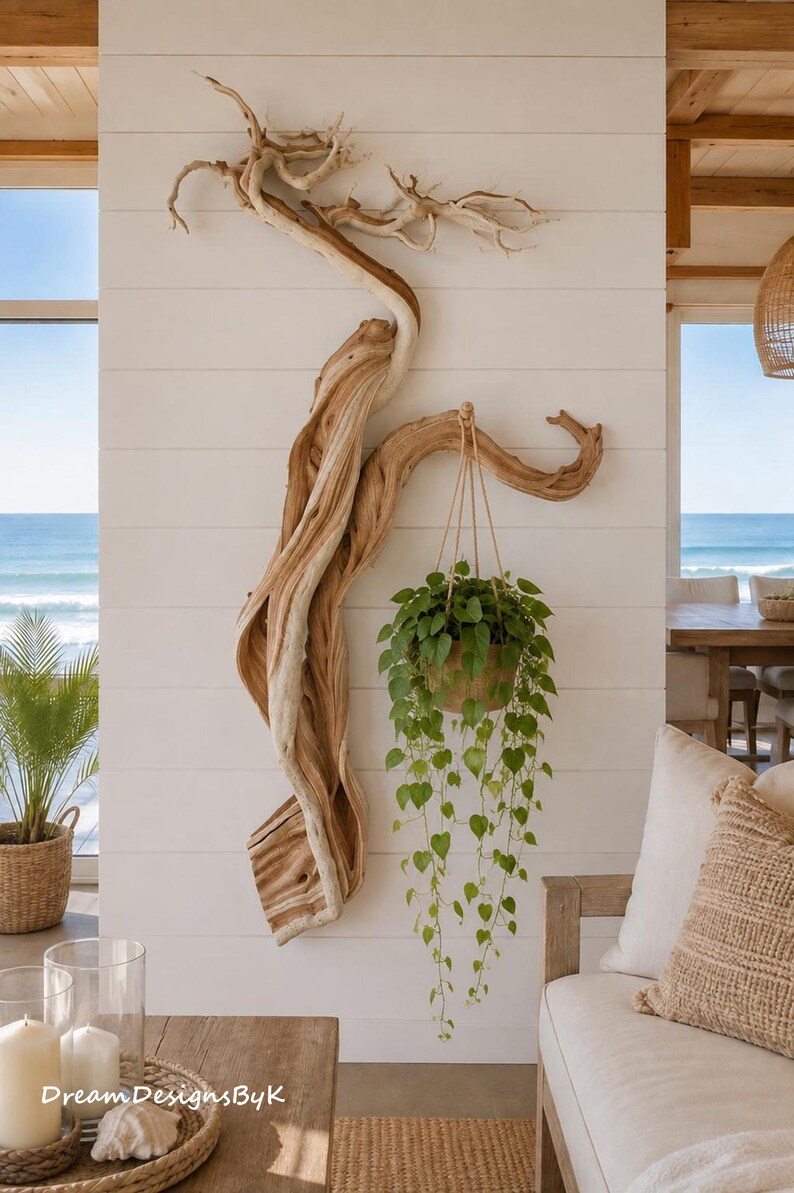May include: A large, light-colored piece of twisted driftwood mounted on a white horizontal plank wall. A green trailing plant in a tan pot hangs from a sturdy branch of the driftwood by a thin rope, creating a natural wall-mounted display.