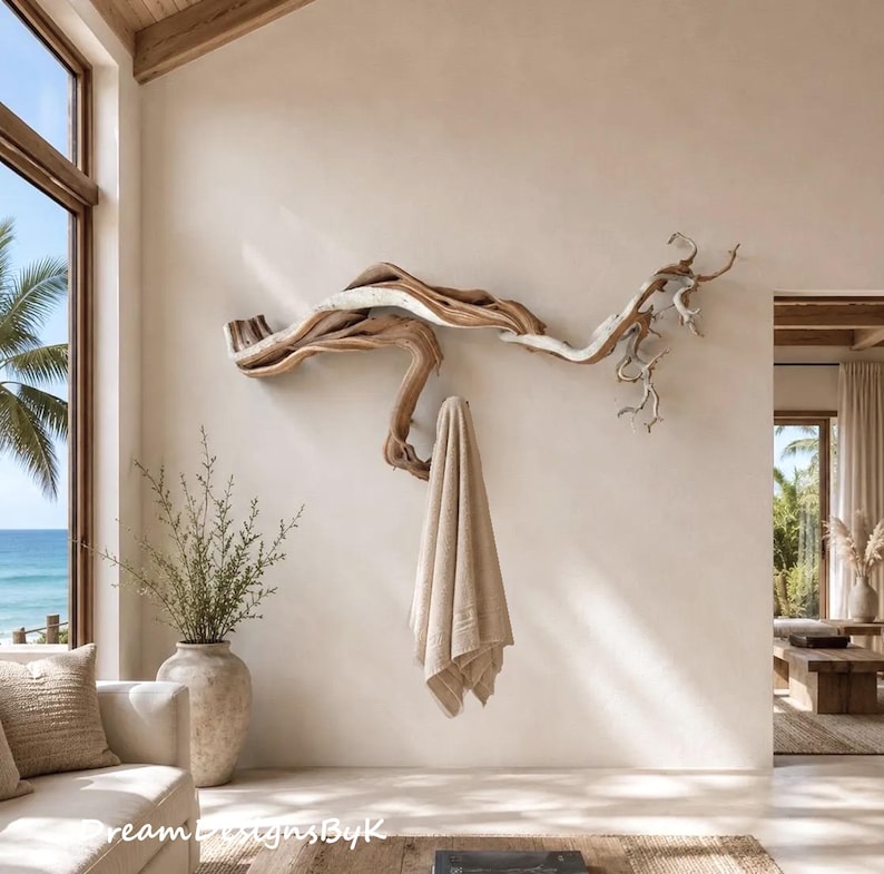 May include: A wall-mounted coat rack crafted from a large, natural piece of light brown driftwood with a smooth, weathered texture. The organic, branching shape of the wood provides multiple hooks for hanging items, with a beige towel draped over it.