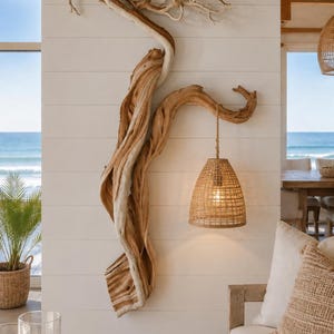 May include: A wall-mounted light fixture featuring a large, natural, twisted piece of driftwood that extends vertically. A woven, bell-shaped rattan lampshade hangs from a sturdy rope attached to a branch of the wood, emitting a warm, soft glow.