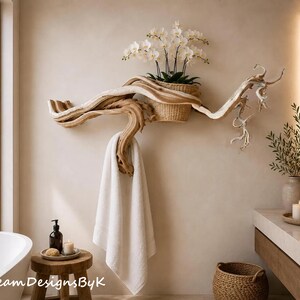 May include: A wall-mounted driftwood towel rack featuring a natural light brown wood grain, a woven basket holding a white orchid plant, and a white towel hanging from a curved branch section. The piece is mounted on a smooth beige wall.