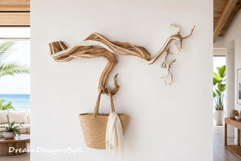 May include: A wall-mounted natural driftwood branch sculpture featuring a horizontal, twisted form with light and dark brown wood grain textures. A woven tan straw tote bag with a white fabric cloth draped over the handle hangs from the branch.