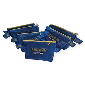 Op de afbeelding: Een verzameling blauwe etuis met ritssluiting, gele ritsen en het woord "IKEA" erop gedrukt. De etuis hebben blauwe en gele bandjes. De etuis zijn gemaakt van een duurzaam, geweven materiaal.