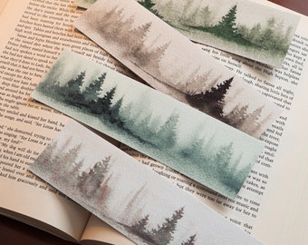 Può includere: Quattro segnalibri ad acquerello con una scena di foresta. Ogni segnalibro presenta una diversa tavolozza di colori, tra cui sfumature di verde, grigio e marrone. I segnalibri sono rettangolari e sembrano fatti a mano.