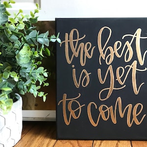 May include: Black canvas with gold lettering that reads "The best is yet to come".
