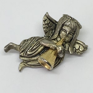 May include: A silver angel figurine with wings, a gold trumpet, and a crown of leaves. The angel is flying and playing the trumpet.
