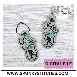 May include: A digital embroidery file for a Bigfoot footprint keychain. The footprint is gray with green accents and features a silhouette of Bigfoot walking through a forest scene with mountains and a lake. The text "DIGITAL FILE" is visible in the image.