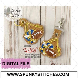 May include: Two cork keychains with a football and cheerleading pom pom design. The keychains are stitched with blue, white, and gold thread. The text "Spunky Stitches" and "stitched by: Ruby" is visible in the image.