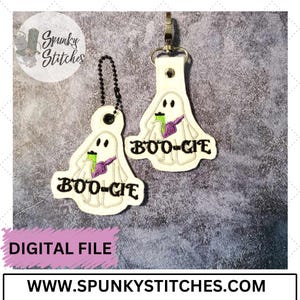 Op de afbeelding: Twee witte geestenvormige sleutelhangers met een paars en groen ontwerp. De geesten houden een groen drankje vast en hebben de tekst "BOO-GIE" erop.