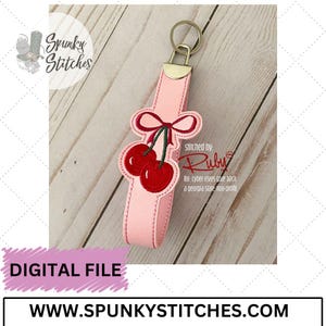 May include: Pink key chain with a red cherry and bow embroidery. The text "Stitched by: Ruby for cyber elves give back a Georgia state non-profit" is on the keychain.