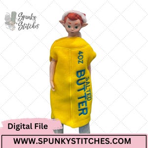 May include: A doll with red hair and pointed ears wearing a yellow felt costume shaped like a stick of butter. The costume features blue embroidered text that reads 4OZ SALTED BUTTER. The doll also wears a small white hat with a red top.