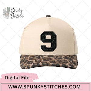 Puede incluir: Gorra de béisbol beige con un parche negro con el número 9. La visera presenta un estampado de animales marrón y beige. La gorra tiene un botón negro en la parte superior. El texto "Digital File" es visible en la parte inferior izquierda.