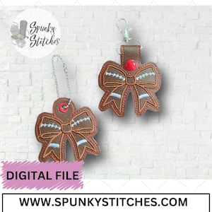 May include: Two brown and white football-themed bow designs. One is a keychain with a red button and the other is a charm with a silver chain. Both designs feature white stitching and a red button in the center.