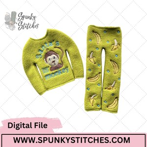 May include: A lime green long-sleeved shirt and matching trousers set. The shirt features an embroidered monkey design with the text "Santa's lil' monkey". The trousers are decorated with banana and blue dot embroidery. The website address is www.SPUNKYSTITCHES.COM.