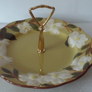 May include: A yellow ceramic serving tray with a gold handle. The tray is decorated with white magnolia flowers and green leaves.