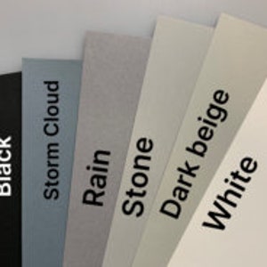 Puede incluir: Un abanico de seis muestras de papel rectangulares en varios tonos de gris, beige y blanco, incluido el negro. Cada muestra tiene una etiqueta con un nombre de color: Black, Storm Cloud, Rain, Stone, Dark Beige y White.