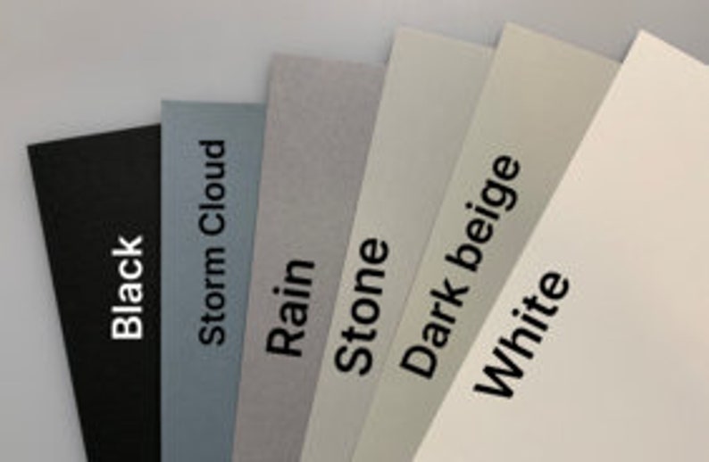 Puede incluir: Un abanico de seis muestras de papel rectangulares en varios tonos de gris, beige y blanco, incluido el negro. Cada muestra tiene una etiqueta con un nombre de color: Black, Storm Cloud, Rain, Stone, Dark Beige y White.